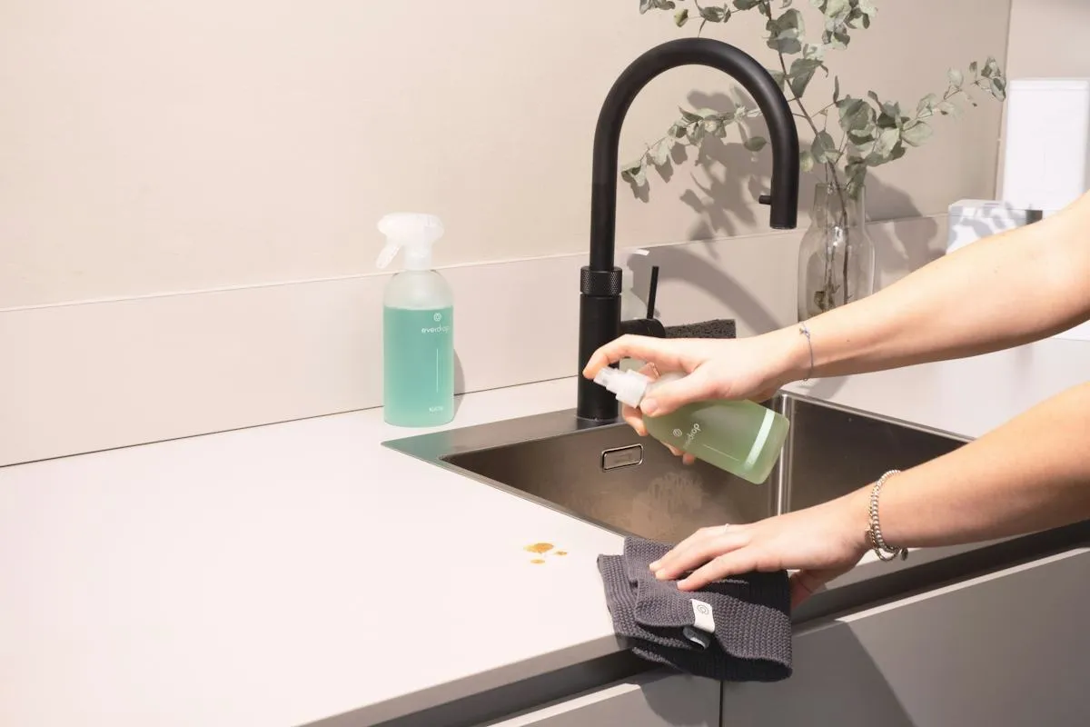 Hands cleaning a kitchen sink with a cloth
